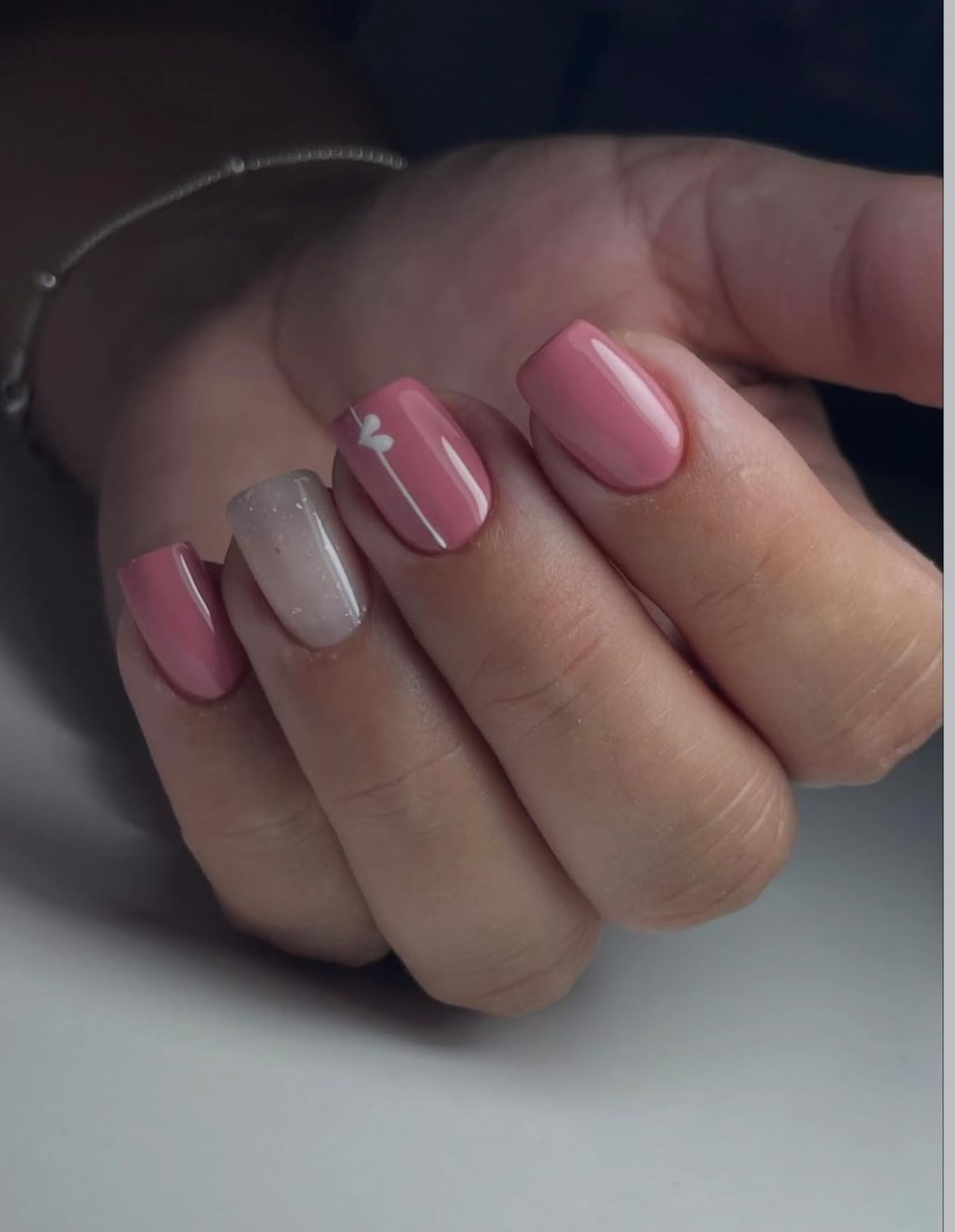 Uñas rosa con un corazón blanco y una uña glitter