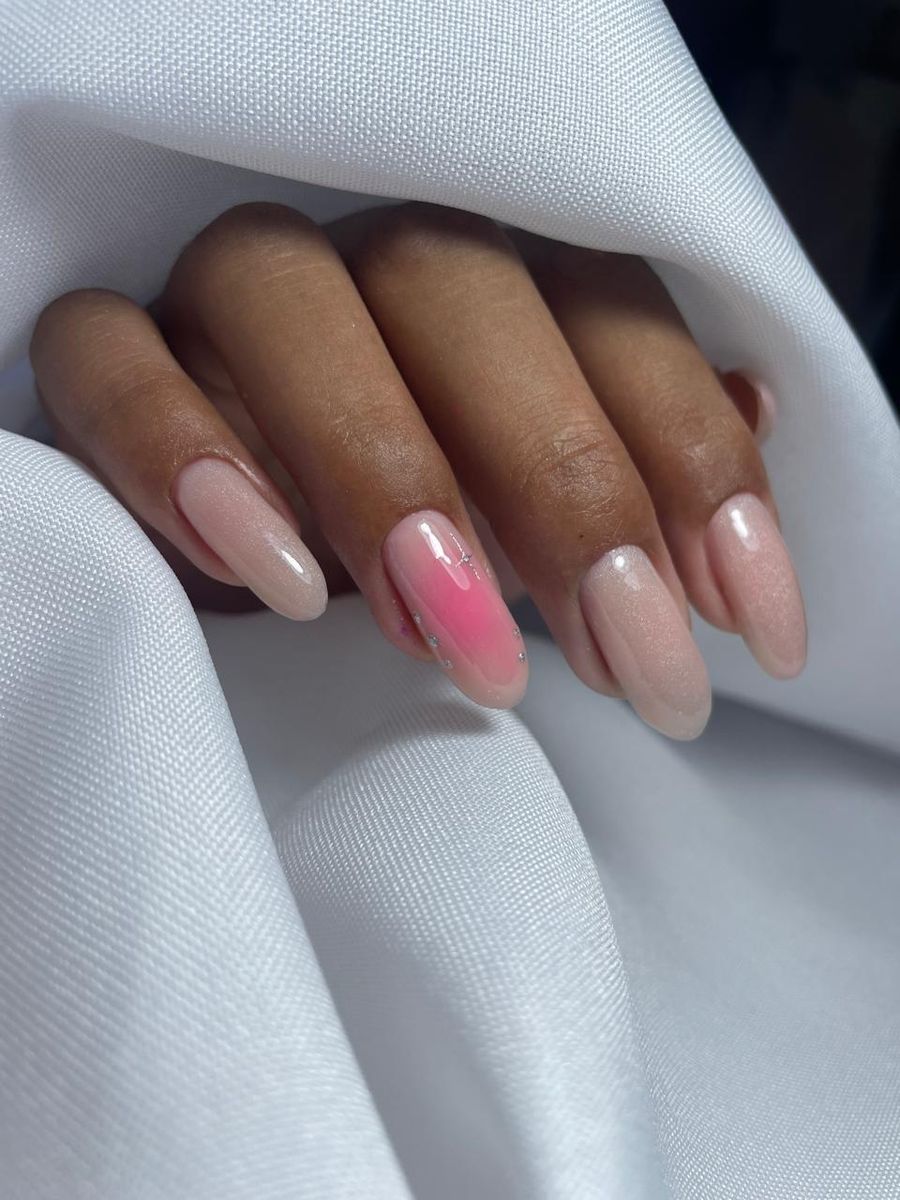 Uñas almendra nude con un aura rosa y brillos